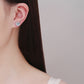 Round halo stud earring worn on an unpierced earlobe, seen over the shoulder of a model