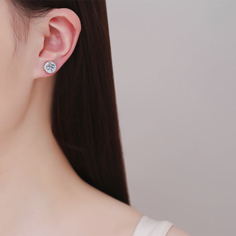 Round halo stud earring worn on an unpierced earlobe, seen over the shoulder of a model
