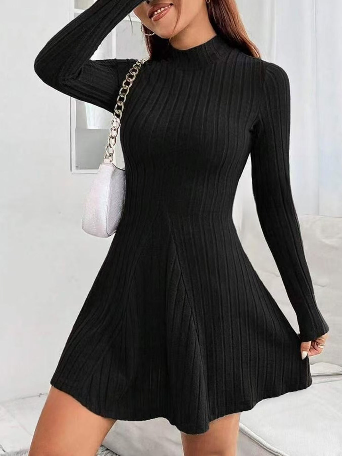 Black ribbed knit mock neck long sleeve fit and flare mini dress worn with a white chain shoulder bag