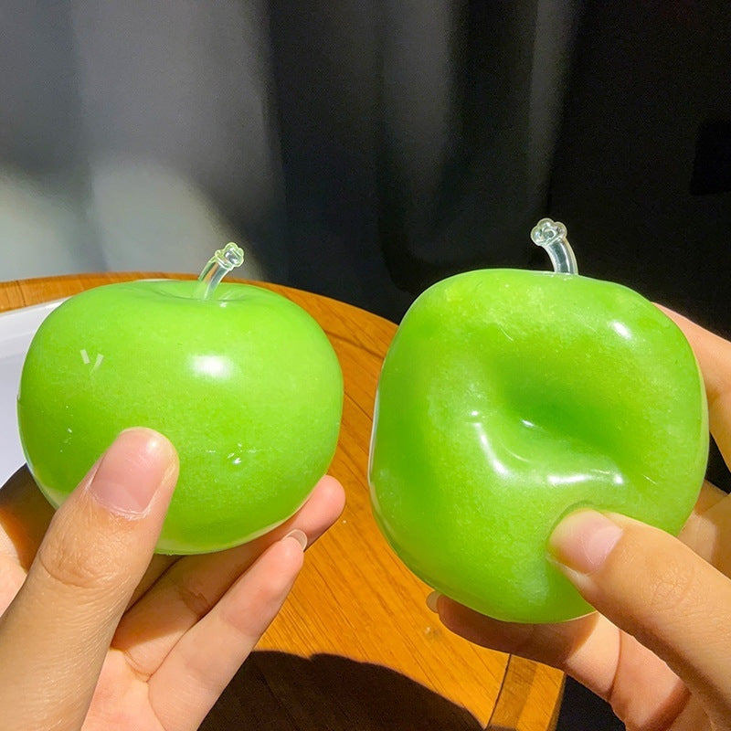 Two green apple squishies held in a hand, the right one keeping a deep pressed crater