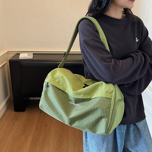 Woman carrying a green duffel shoulder bag with a grid textured lower panel over a dark sweater and jeans