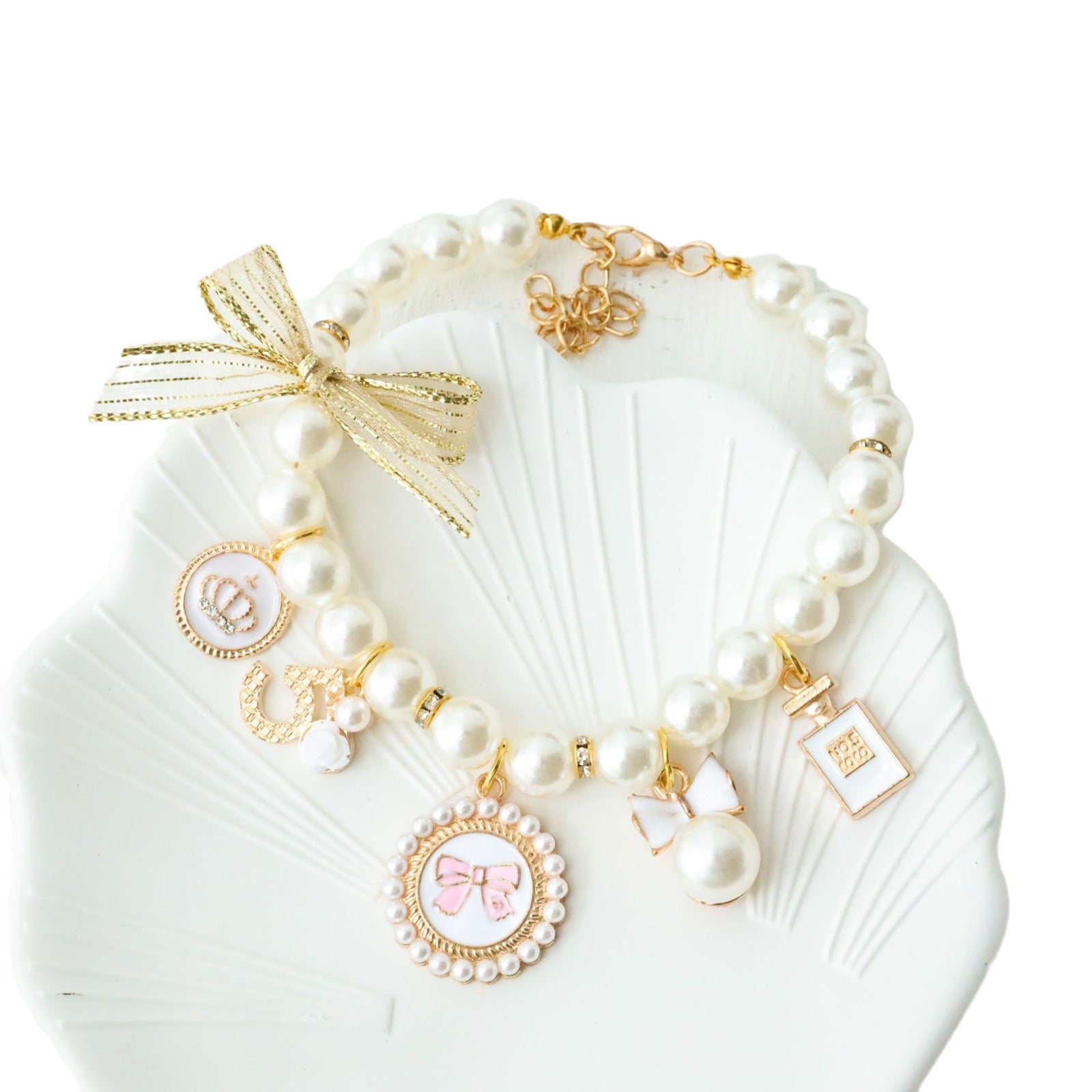 White faux pearl pet necklace collar with bow cameo and perfume bottle charm on a shell tray