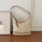 Open weave cream shoulder bag with tan stripes shown against a plain wall