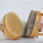 Two oval body brushes on a white towel, one with cream boar bristles and one with grey horsehair bristles