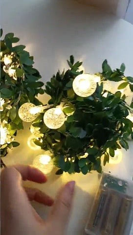 Bubble flower LED fairy string light on a green leaf vine with a warm glow, decorative photo