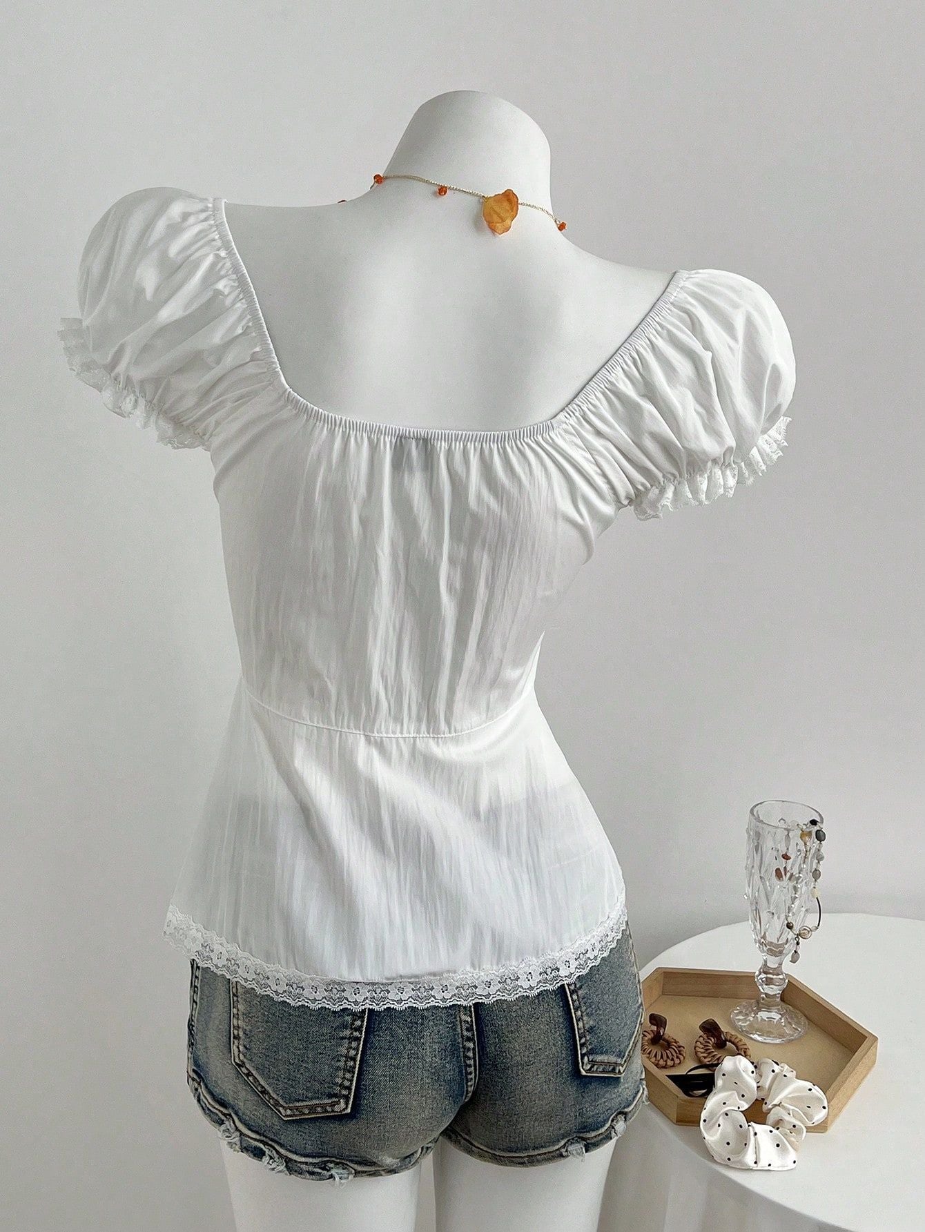 Back view of the white blouse on a dress form, plain gathered back, waist seam and scalloped lace hem