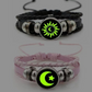 Both cord bracelets in the dark with the sun and moon motifs glowing green against the black cabochons