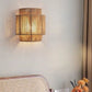 Hemp rope wall lamp glowing warm white on a wall behind a cane chair back, curtain and orange flowers