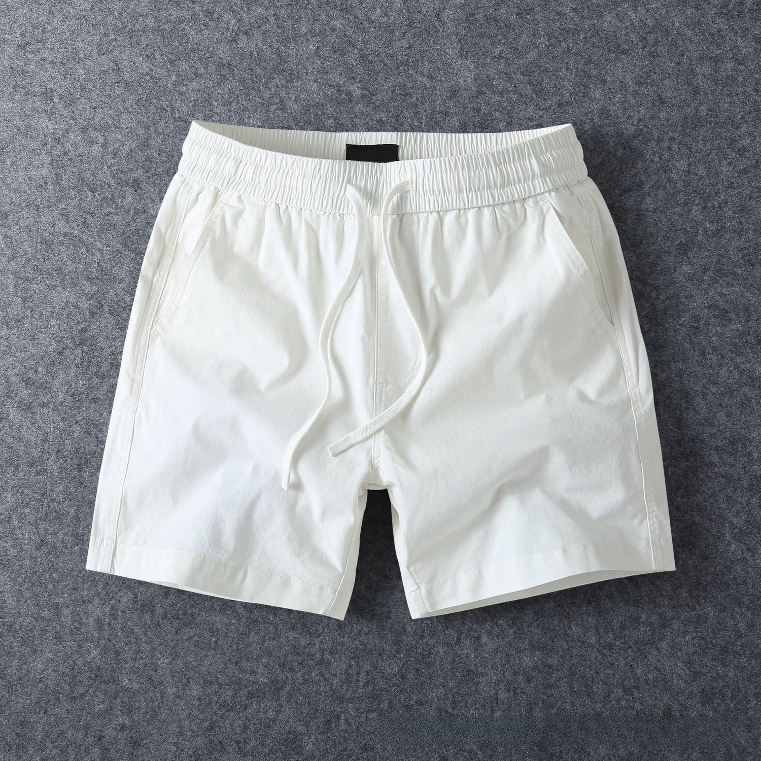 White men's cotton drawstring shorts in a full flat lay on a grey studio backdrop