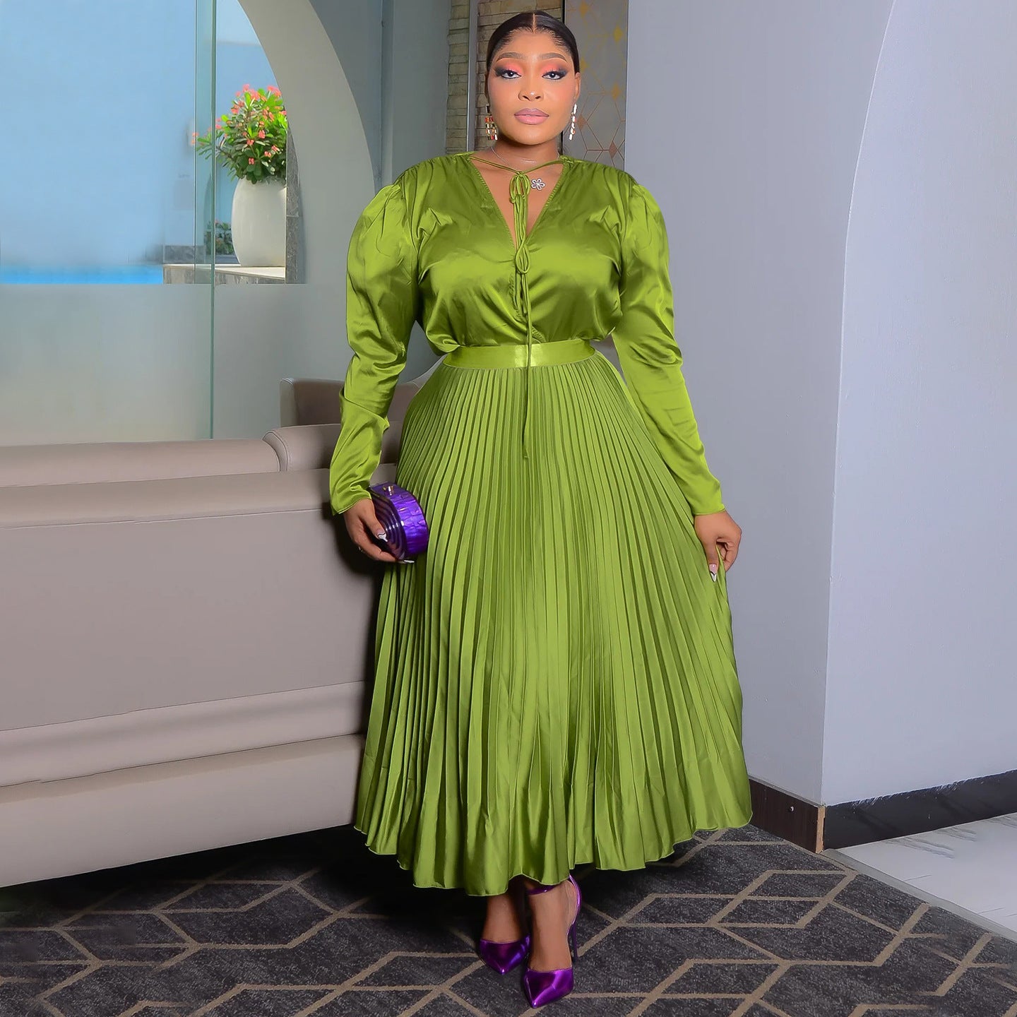 Olive green high shine pleated maxi dress with tie neck and matching belt, worn indoors
