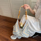 Blue and white open-weave hobo bag held by the beaded cord handle, tulips inside, over a wood floor