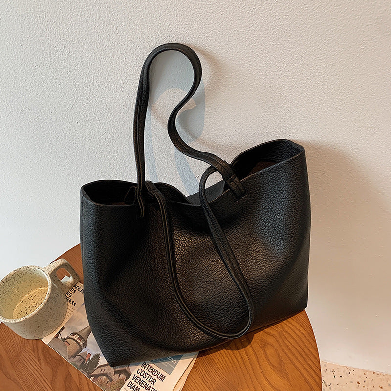 Black PU tote bag with a long strap loop hanging above a wooden stool and a mug, Black option photo