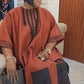 Close view of an orange red boubou neckline showing the black striped placket beaded tassels and sequin cuff