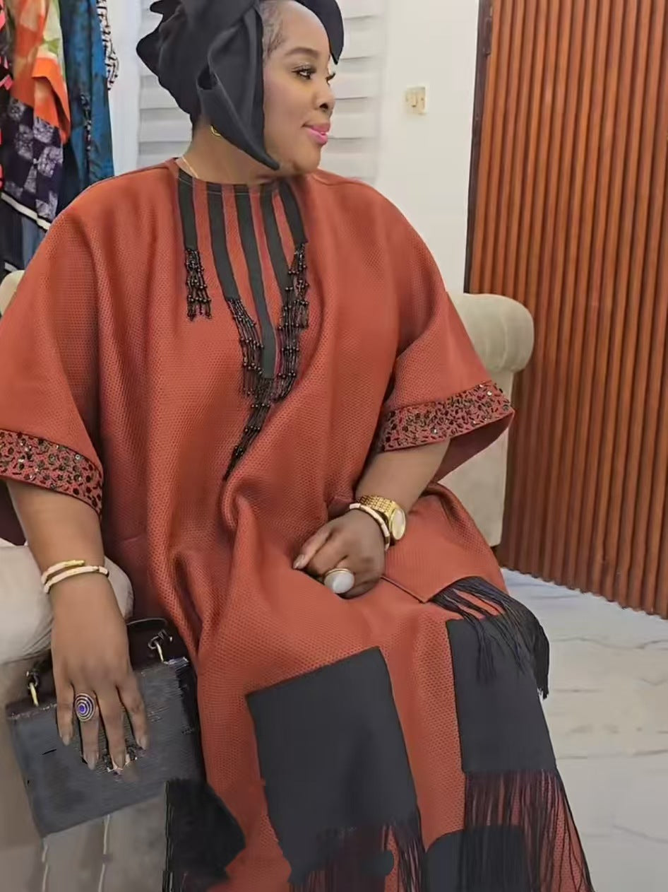 Close view of an orange red boubou neckline showing the black striped placket beaded tassels and sequin cuff