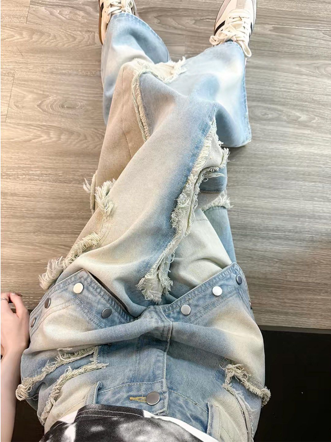 Washed blue wide leg baggy jeans with raw frayed appliques worn by a woman, streetwear styling