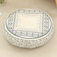 Round cushion with a navy square frame print on a cream top and a navy patterned side, on a beige rug