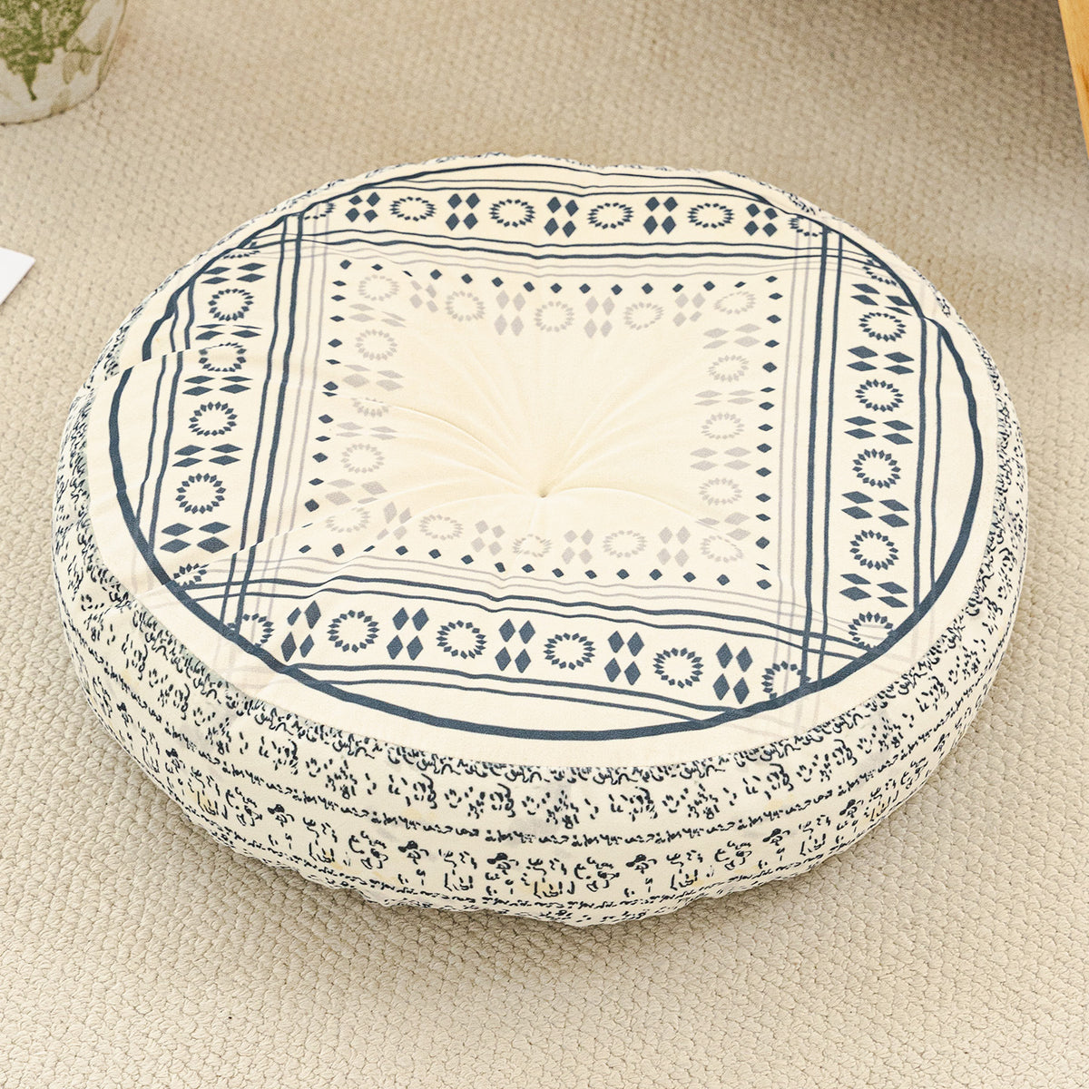 Round cushion with a navy square frame print on a cream top and a navy patterned side, on a beige rug