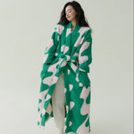 Woman wearing a long green and pale pink wavy print fleece robe with a belt over cream trousers, full length view