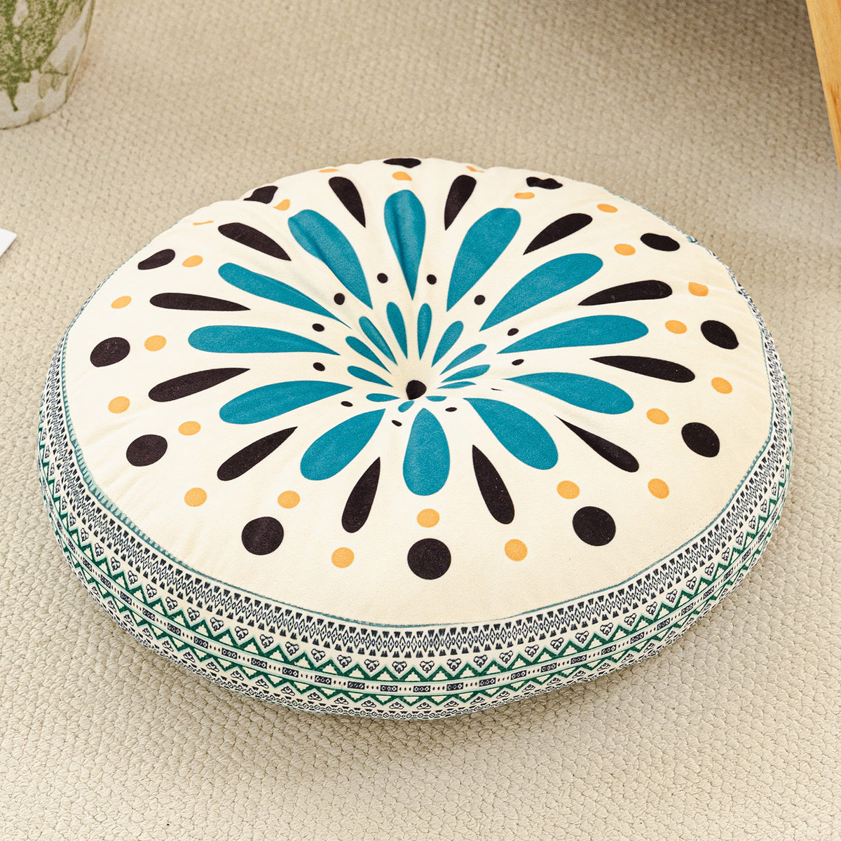Round cushion with teal petals and black and yellow dots on a cream top with a teal green woven border
