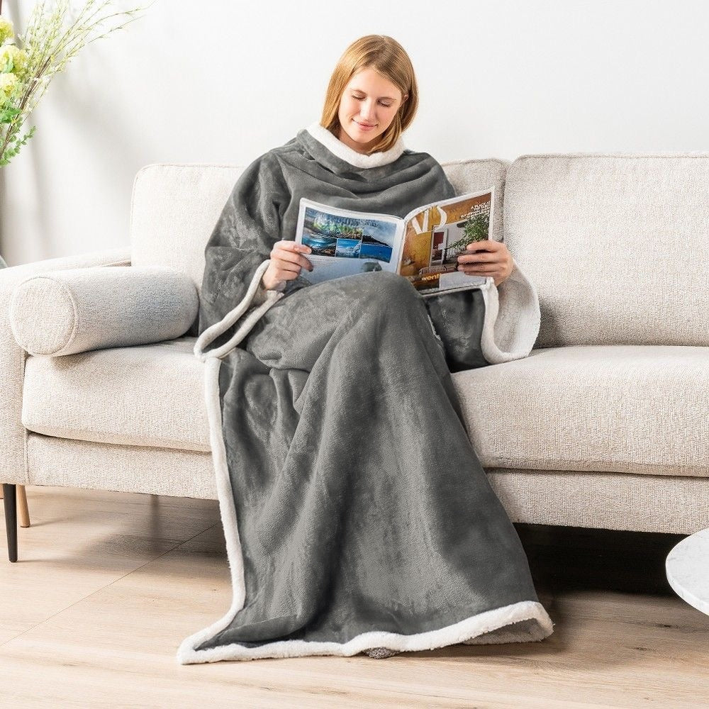 Woman reading on a sofa in a gray sleeved flannel blanket with white sherpa trim, Gray option