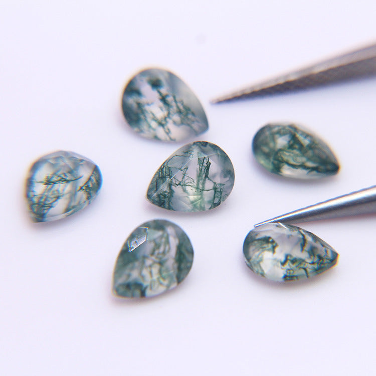 Six moss agate pears on white with steel tweezers, faceted crowns catching the light