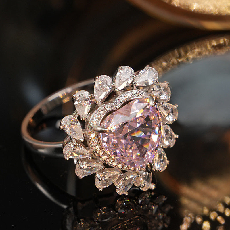 Large pink heart stone ring ringed with pear cut clear accents, photographed on a dark gold toned setting