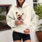 Woman in a cream fleece hoodie with a small dog peeking out of the front pouch pocket