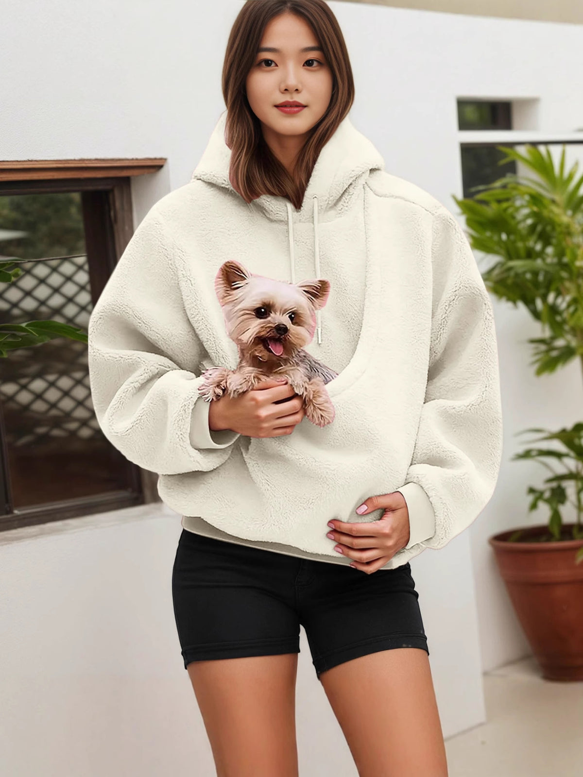 Woman in a cream fleece hoodie with a small dog peeking out of the front pouch pocket