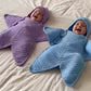 Purple and blue crochet star hooded baby buntings worn by two babies lying on a bed