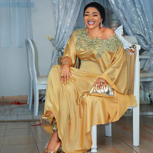 Gold satin flowing maxi dress with a wide lace neckline and long draped sleeves