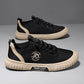 Pair of black lace up canvas sneakers with a beige ribbed sole and a beige heel stripe on a gray backdrop