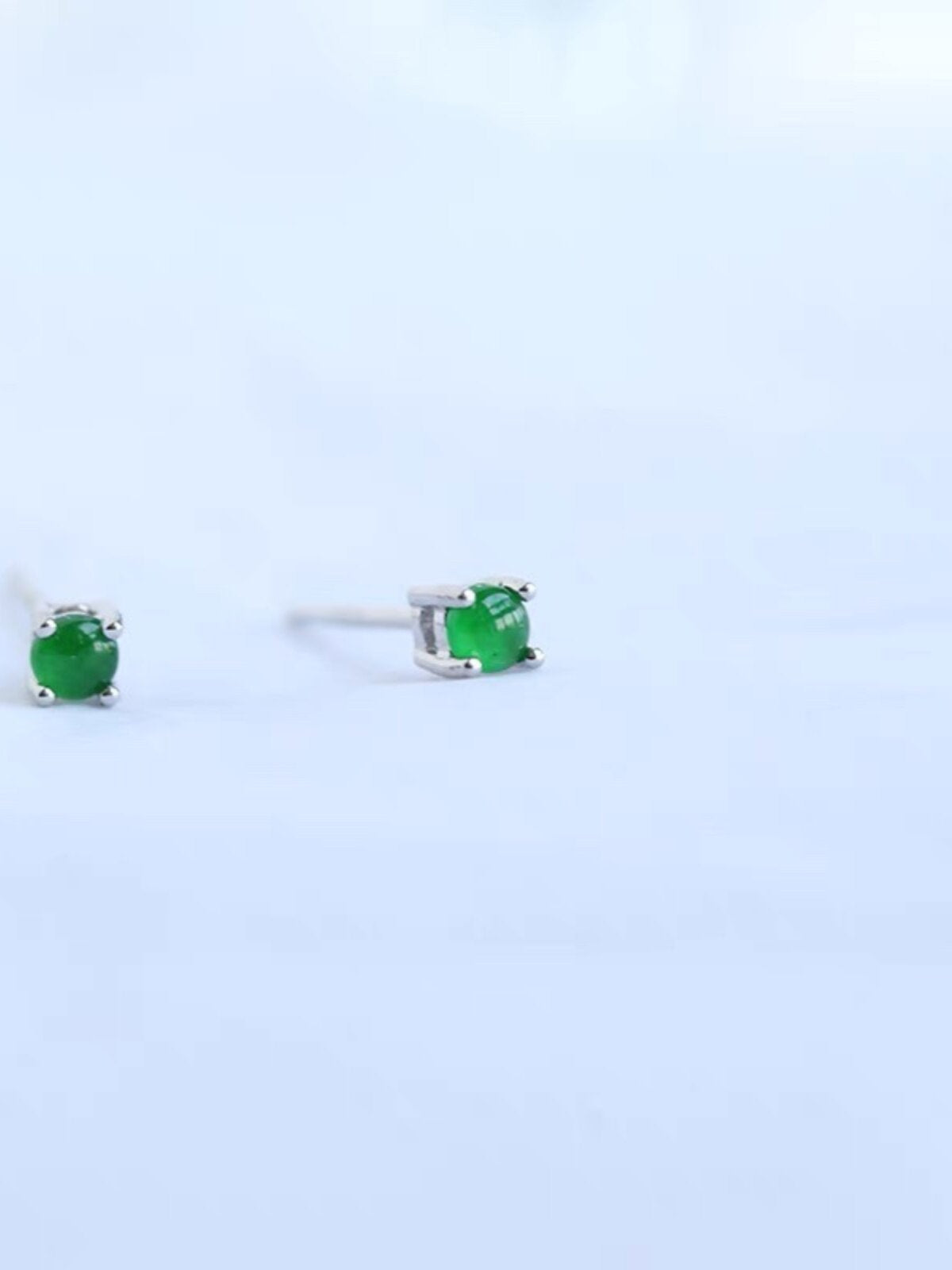 Side view of two green cabochon studs showing the straight posts and friction push backs on a hand