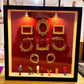 Black frame red backdrop shadow box lit by two spotlights with empty gold frames and small figurines on the ledge