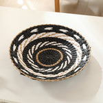 Hand-woven straw wall decor disc with a black and white coiled spiral pattern