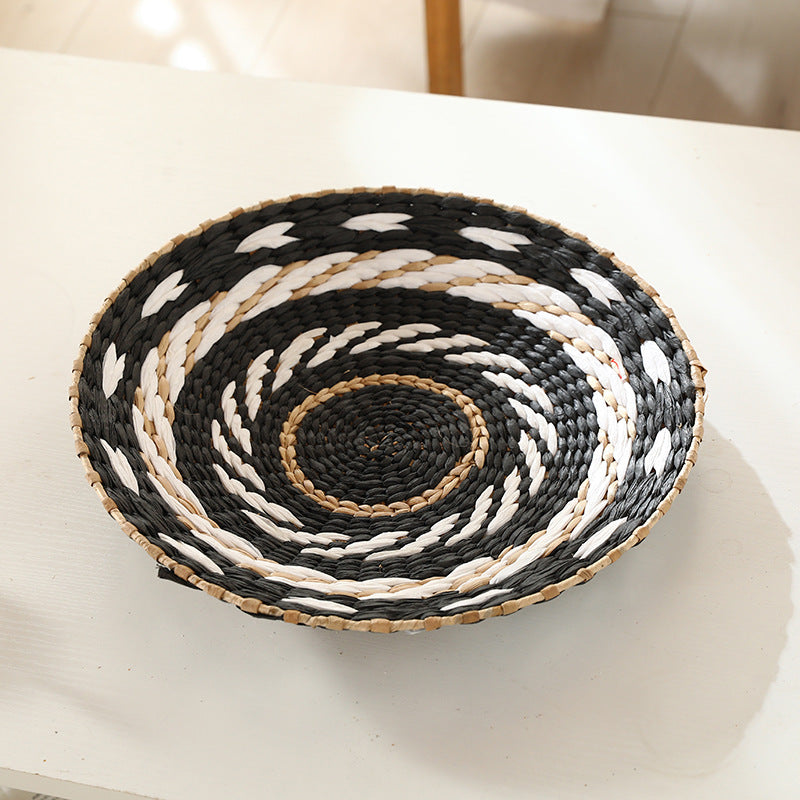 Hand-woven straw wall decor disc with a black and white coiled spiral pattern