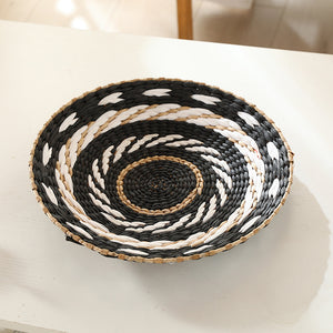 Hand-woven straw wall decor disc with a black and white coiled spiral pattern