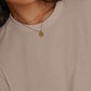 Close up of the round neck and narrow finished edge on a khaki rayon top with a pendant necklace