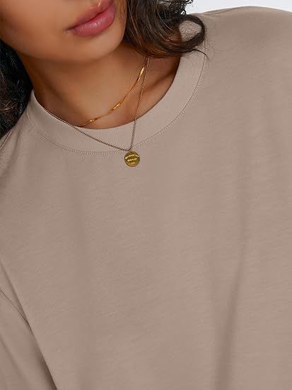 Close up of the round neck and narrow finished edge on a khaki rayon top with a pendant necklace