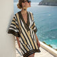 Loose V neck bohemian beach cover up dress in a blue and orange sun motif print, worn against a sunlit coastal wall