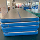 Stack of blue inflatable air track mats with a gray top and a blue center stripe in a factory