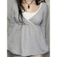 Woman in a gray long sleeve crossover V neck top with lace edging, worn over a white lace camisole with a small bow