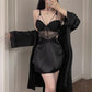 Black nightdress with lace bodice, center bow and cross straps worn with a lace-cuff black robe, model standing