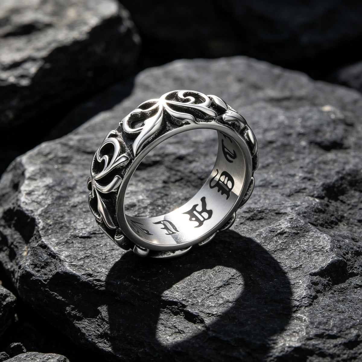 Size US 10 option photo of the silver gray scrollwork band ring on dark rock with engraved lettering inside