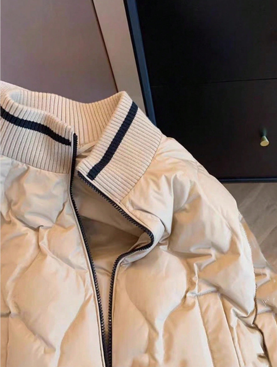 Close view of the ribbed stand collar and black stripe on a khaki quilted bomber jacket