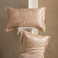 Pair of peach floral jacquard silk pillowcases, one lying flat and one propped on a column