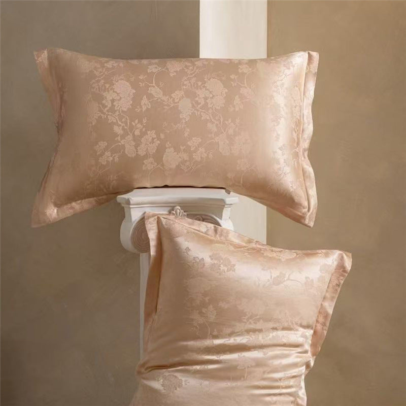 Pair of peach floral jacquard silk pillowcases, one lying flat and one propped on a column