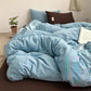 Blue and coral striped cotton bedding set unmade on a bed with a brown fitted sheet, seen from the side