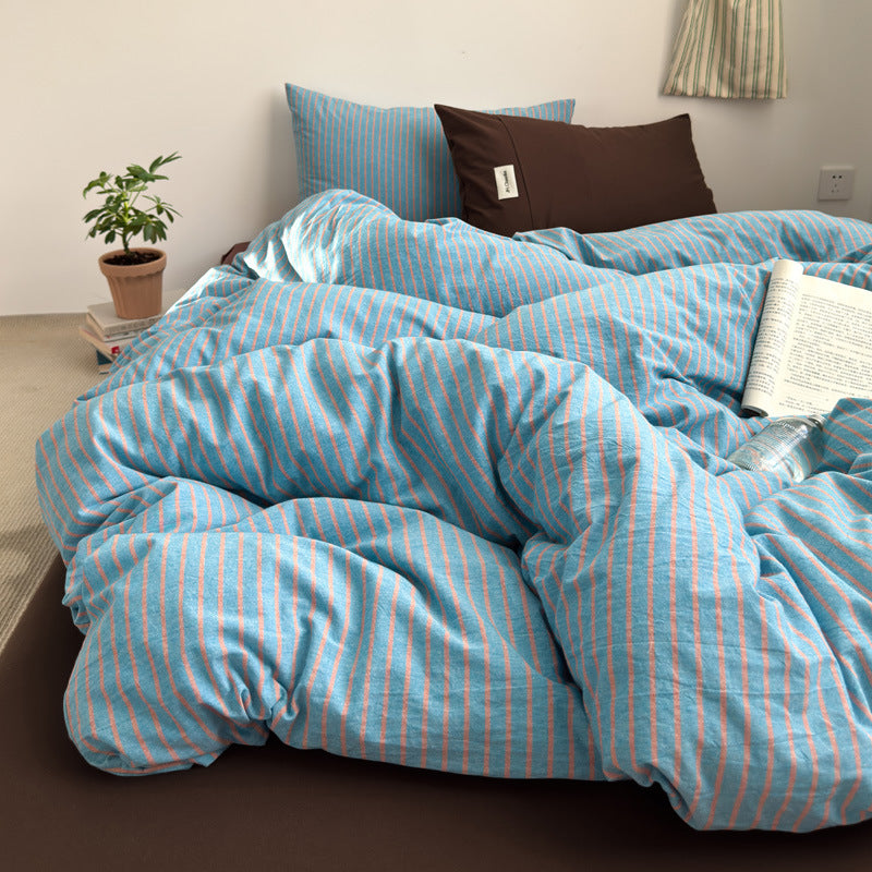 Blue and coral striped cotton bedding set unmade on a bed with a brown fitted sheet, seen from the side