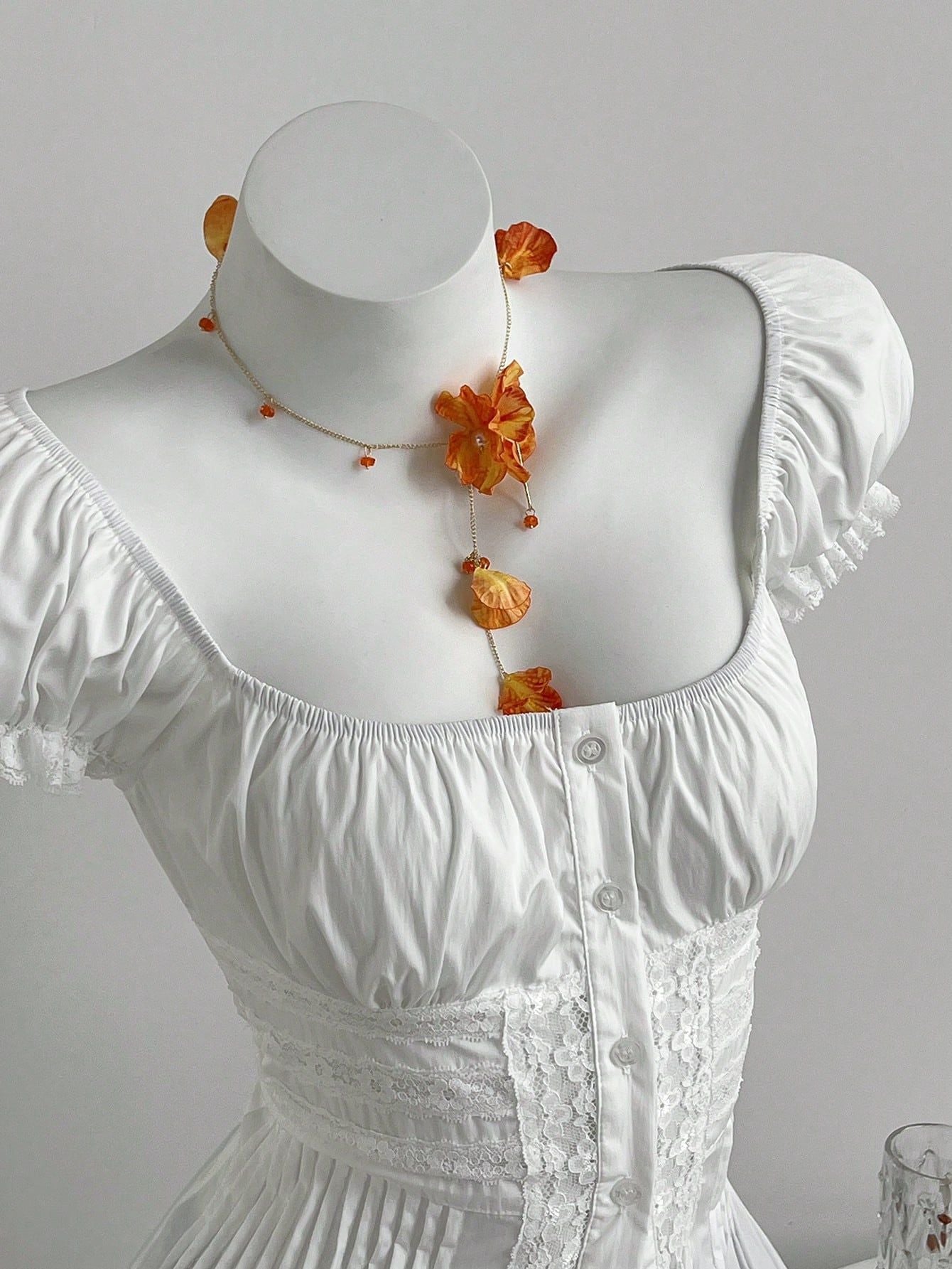 Close up of the square elasticated neckline and puff sleeve caps of the white collarless blouse