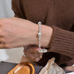 Hand adjusting the silver beaded bracelet at the wrist, brushed bead catching the light